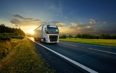 White truck driving on the asphalt road in rural landscape in the rays of the sunset