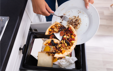 Reste einer Pizza werden mit einer Gabel in den Müll geschmissen.